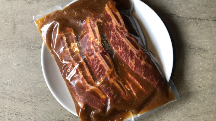 korean kalbi beef short ribs marinating in a ziplock bag on a white plate